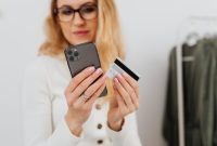 Seorang wanita mempertimbangkan keputusan belanja dengan cermat saat melihat berbagai penawaran di aplikasi ponsel pintar miliknya.