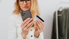 Seorang wanita mempertimbangkan keputusan belanja dengan cermat saat melihat berbagai penawaran di aplikasi ponsel pintar miliknya.