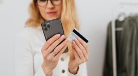 Seorang wanita mempertimbangkan keputusan belanja dengan cermat saat melihat berbagai penawaran di aplikasi ponsel pintar miliknya.