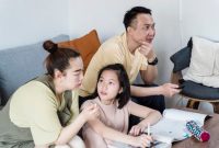 Seorang ibu mendampingi putrinya belajar dengan penuh kesabaran di meja belajar rumah yang tertata rapi. Suasana yang tenang dan penuh kasih sayang terbukti meningkatkan fokus serta kepercayaan diri anak.