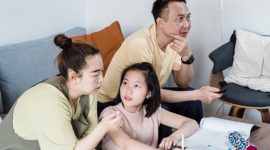 Seorang ibu mendampingi putrinya belajar dengan penuh kesabaran di meja belajar rumah yang tertata rapi. Suasana yang tenang dan penuh kasih sayang terbukti meningkatkan fokus serta kepercayaan diri anak.